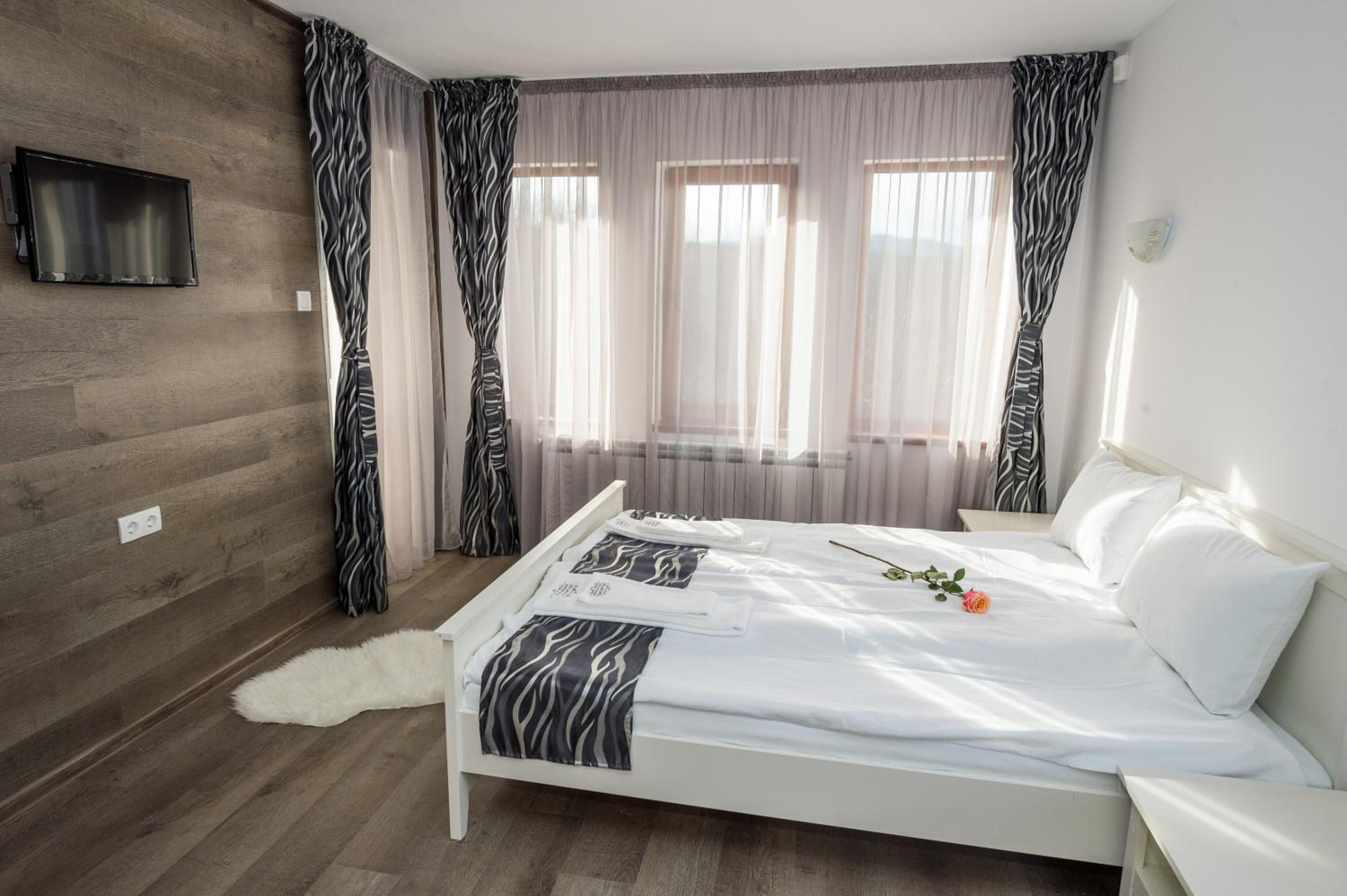 A bedroom with a bed, a white sofa, a television on the wall, and a window with curtains.