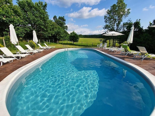 A rectangular swimming pool with clear blue water, surrounded by white lounge chairs and umbrellas, set against a backdrop of trees and a clear sky. - Sinjirite Complex (Elena)