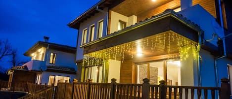 A two-story house with a wooden deck and string lights.