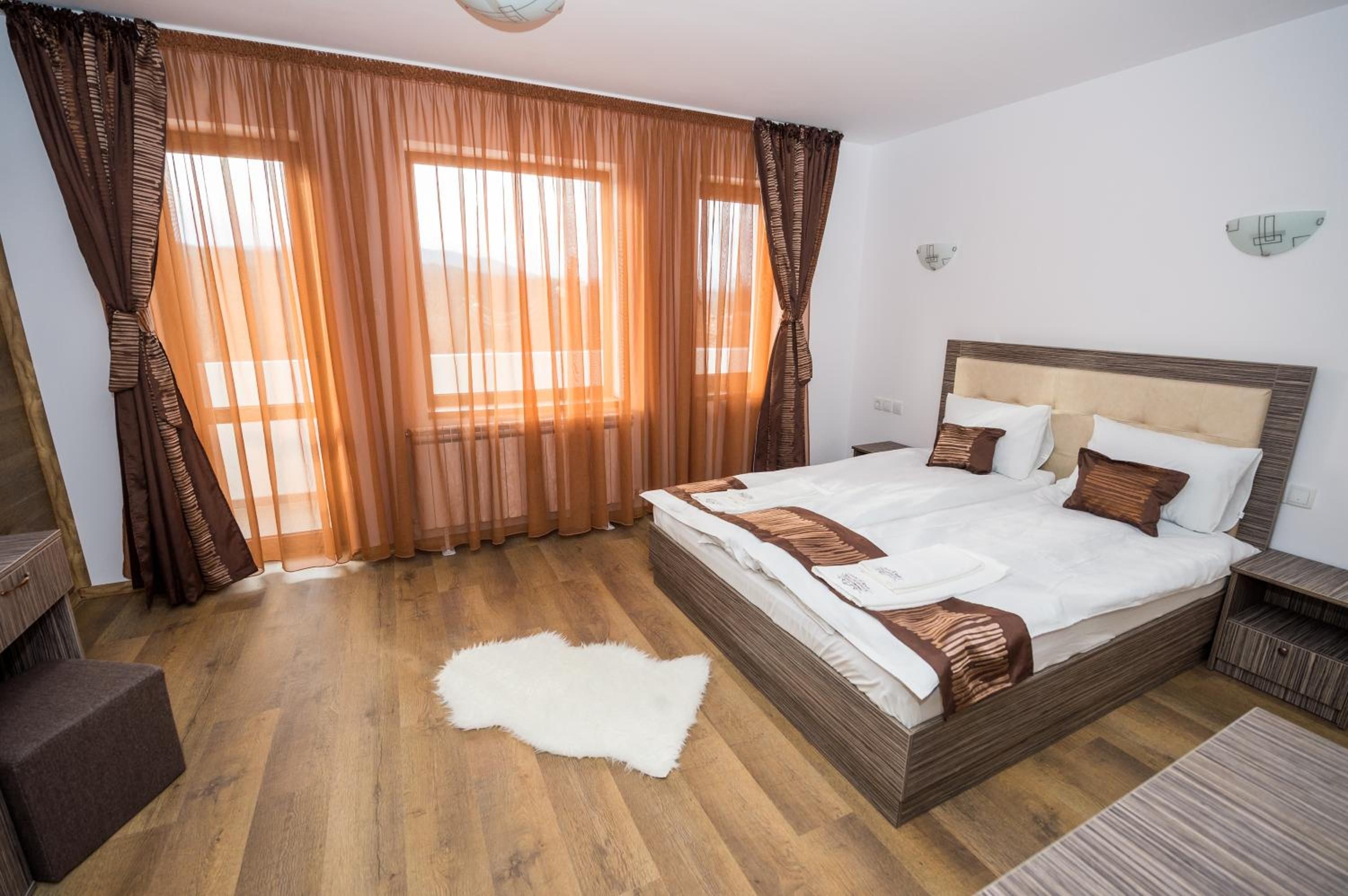 A hotel room with a large bed, wooden flooring, and curtains.