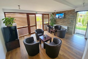 A modern lounge area with a flat-screen TV, comfortable seating, and a stone accent wall. - Sinjirite Complex (Elena)