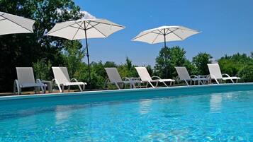 A swimming pool with white lounge chairs and umbrellas.