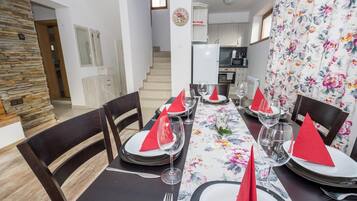 A dining area with a table set for four, chairs, a kitchen in the background, and a staircase leading to another floor.