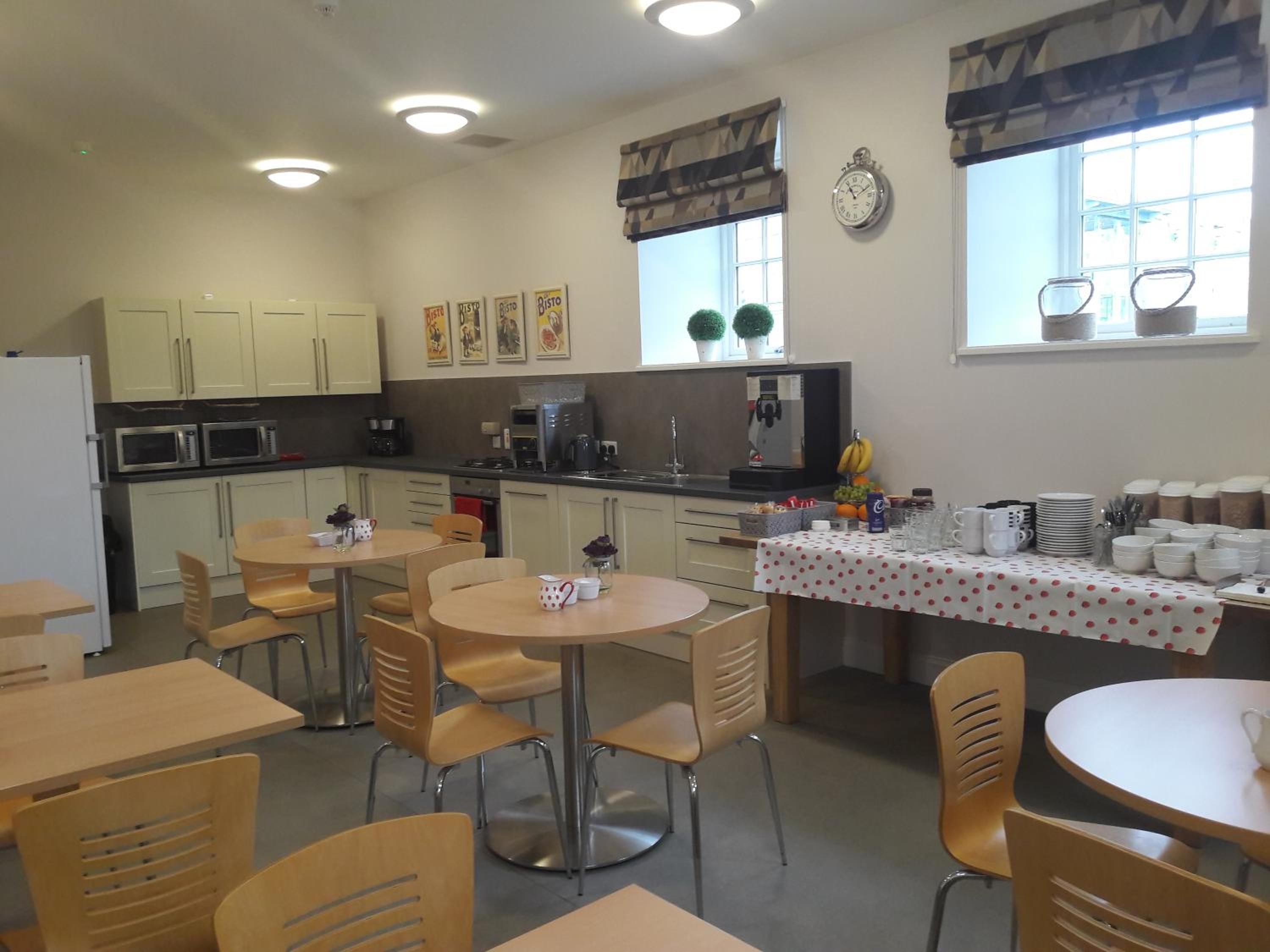 A kitchen with dining tables and chairs, a coffee machine, and a clock on the wall.