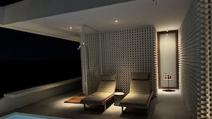 A modern outdoor lounge area with two lounge chairs, a small table, and a pool. - Pousada Mestizo (Touros)