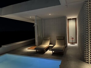 A modern outdoor lounge area with two lounge chairs, a small table, and a pool. - Pousada Mestizo (Touros)