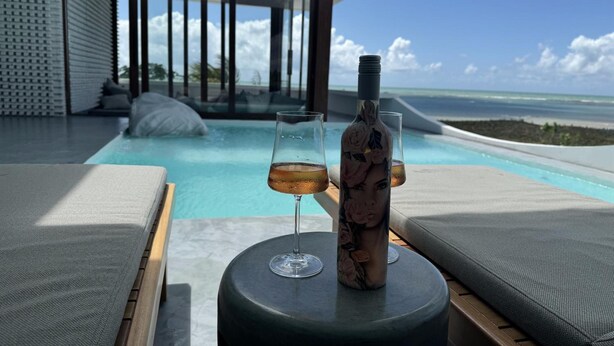 A poolside area with lounge chairs, a bottle, and a glass of drink. - Pousada Mestizo (Touros)