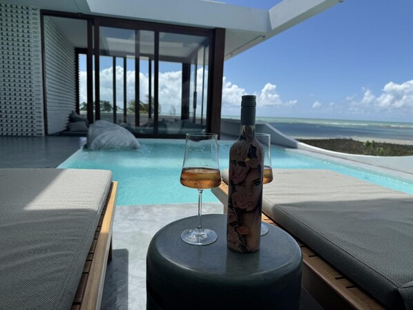 A poolside area with lounge chairs, a bottle, and a glass of drink. - Pousada Mestizo (Touros)