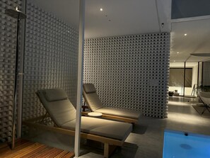 Uma área de spa moderna com duas espreguiçadeiras, piso de madeira e parede com textura.