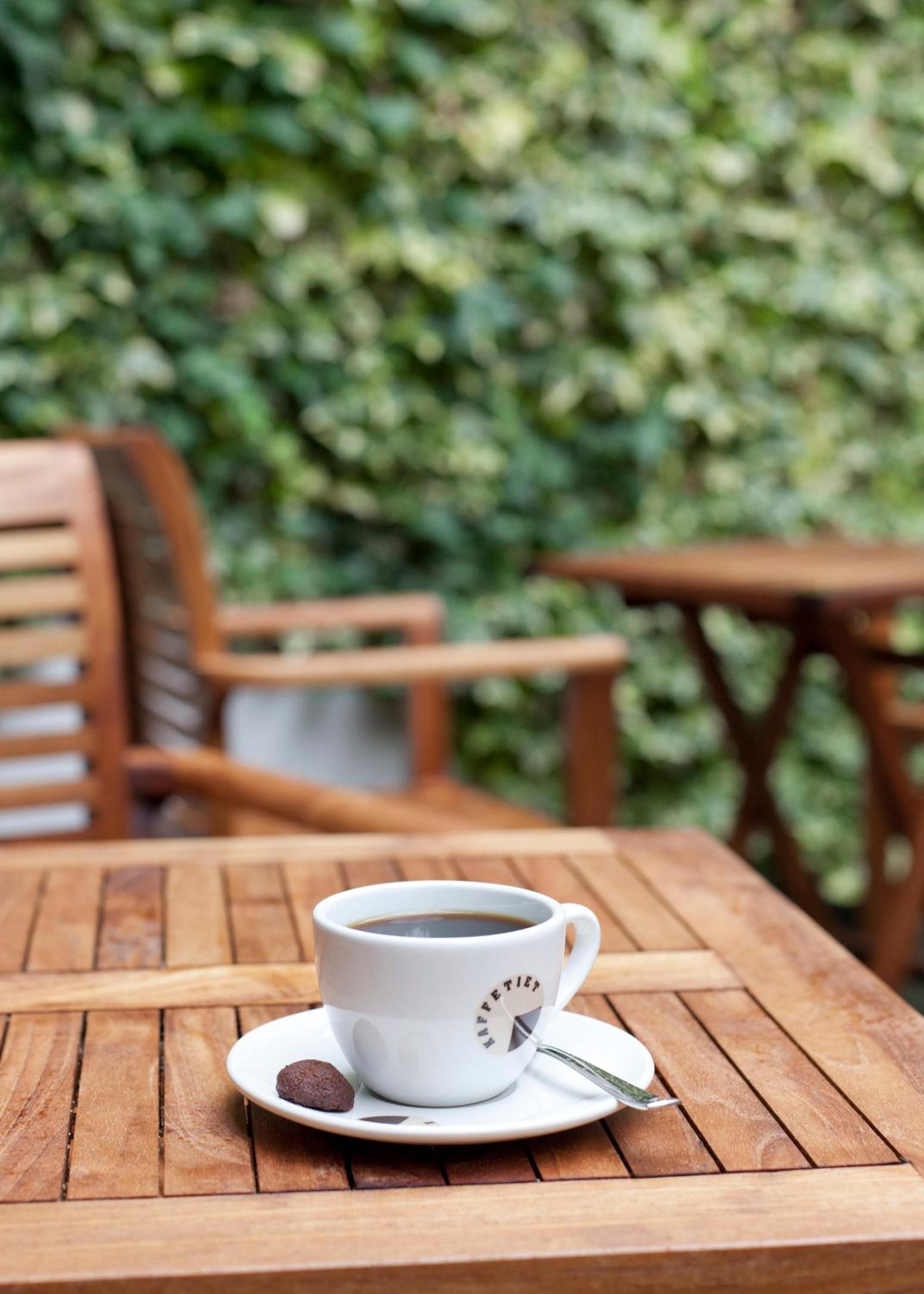 Eine weiße Kaffeetasse mit Löffel auf einem Holztisch im Freien.