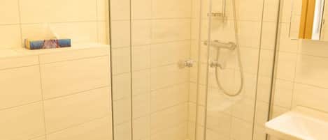 A shower with glass doors, a toilet, and a sink in a bathroom with white tiles.