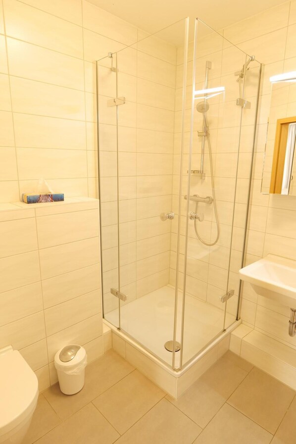 Ducha con puertas de cristal, inodoro y lavabo en un baño con azulejos blancos.