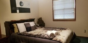 A bedroom with a bed, pillows, a blanket, a teddy bear, a window with blinds, and a painting on the wall. - Wanita's Retreat (Big Bear Lake)