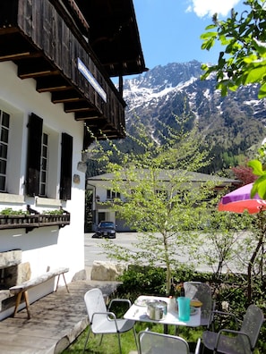 A mountain view with a wooden building, outdoor seating, and a table with chairs. - Gotthard Backpacker (Wassen)