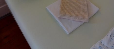 A small, single-bed room with a green pillow and a folded towel on the bed.