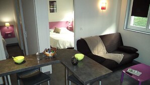 A compact living space with a kitchenette, a dining area, a sofa, and a small table. - West Appart' Hôtel (Bessines)