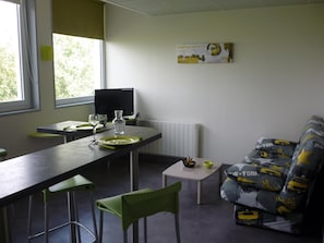 A dining area with a table set for two, a television, and a couch with patterned cushions. - West Appart' Hôtel (Bessines)