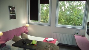 A small, cozy room with a bed, a table, and a window with a view of greenery. - West Appart' Hôtel (Bessines)