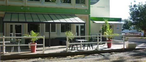 A hotel with a covered outdoor seating area, a green awning, and a sign indicating 'WEST Appart Hotel.'