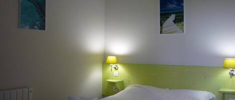 A hotel room with a bed, two wall-mounted lamps, and two framed pictures.