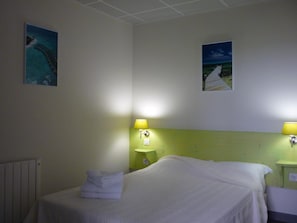 A hotel room with a bed, two wall-mounted lamps, and two framed pictures. - West Appart' Hôtel (Bessines)