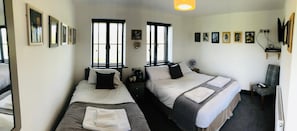 A hotel room with two beds, a bedside table with a lamp, a chair, a desk with a computer, and a wall-mounted TV. - The Players Golf Club (Bristol)