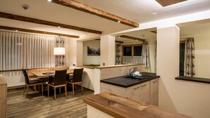Una cocina moderna con vigas de madera, una zona de comedor con mesa y sillas, y un ventanal con cortinas.