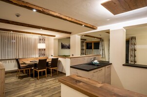 Una cocina moderna con vigas de madera, una zona de comedor con mesa y sillas, y un ventanal con cortinas.