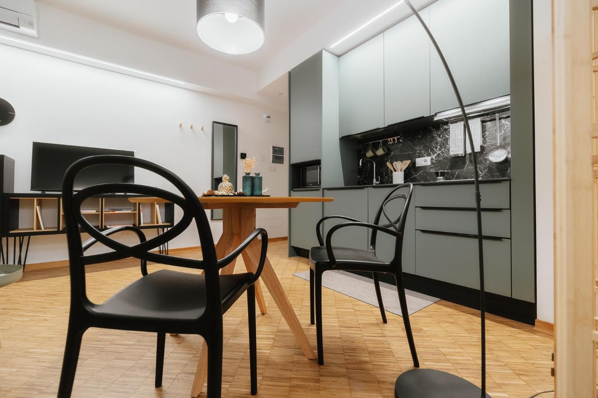 Eine moderne Küche mit grauen Schränken, einer schwarzen Arbeitsplatte und einer Mikrowelle. Zwei schwarze Stühle und ein Holztisch sind ebenfalls vorhanden.