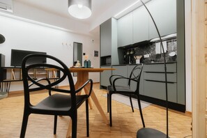 A modern kitchen with grey cabinets, a black countertop, and a microwave. There are two black chairs and a wooden dining table.