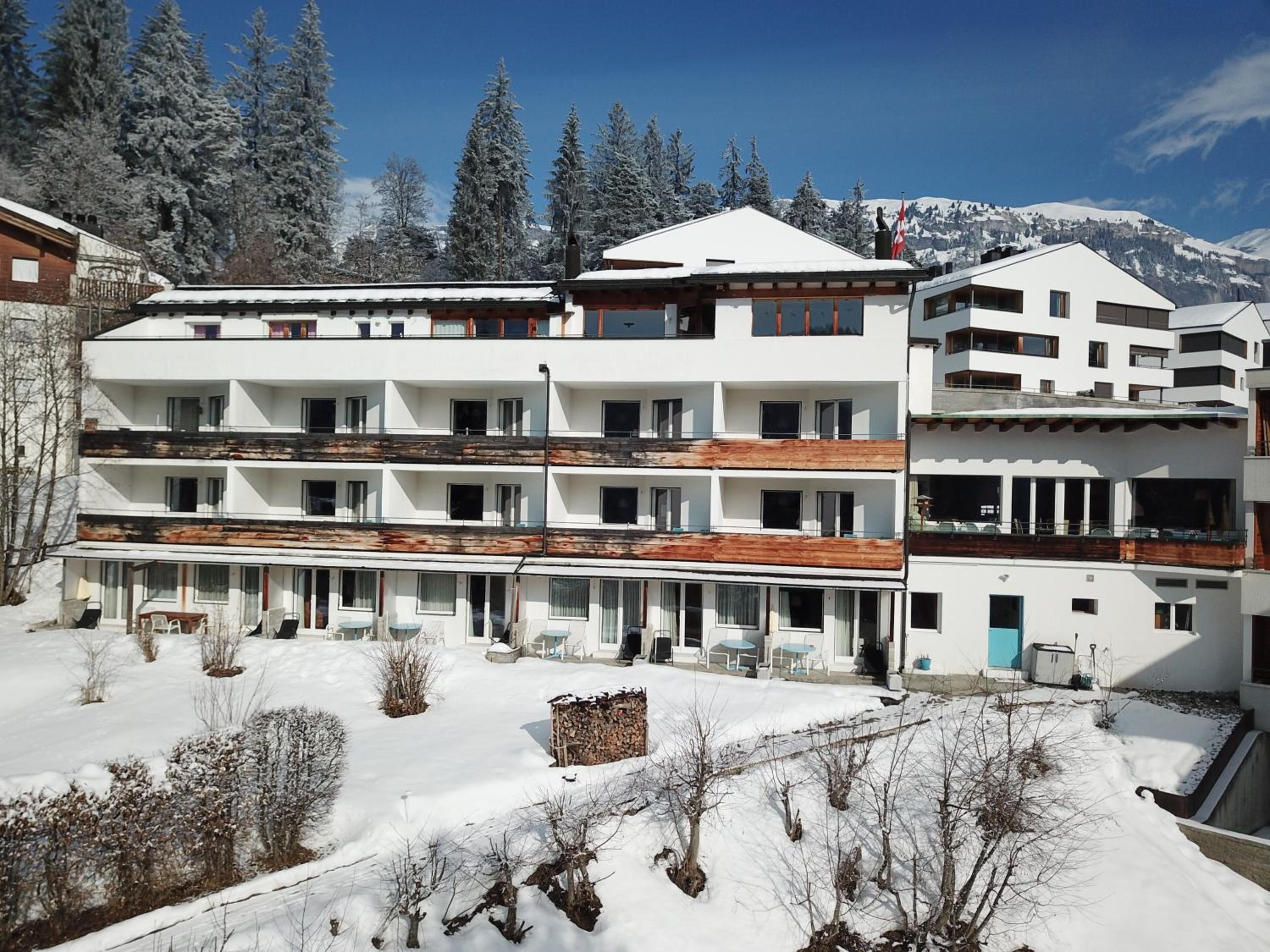 Un hôtel à plusieurs étages doté de balcons, un paysage enneigé et une chaîne de montagnes en arrière-plan.