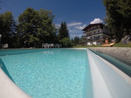 Una piscina cristalina con sillones de descanso y un edificio al fondo.