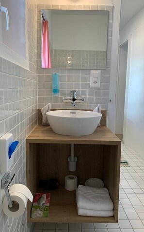 Un baño con un lavamanos blanco, un espejo encima y un mueble de tocador de madera.