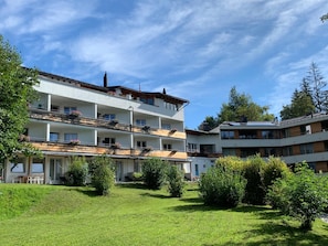 Un hotel de varios pisos con balcones, un patio con césped y árboles circundantes.