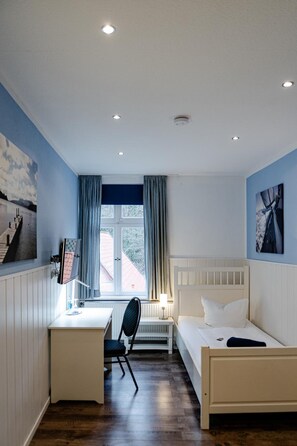 Een slaapkamer met een bed, bureau, stoel en een raam met gordijnen.