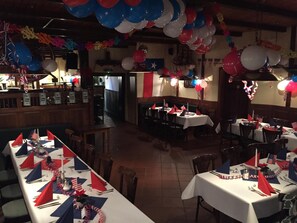 Een restaurant met gedekte tafels, versierd met rood, wit en blauw linnen en ballonnen.