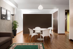 A modern dining area with a round table and white chairs, a potted plant, and a green area rug. - Residence San Martino (Messina)
