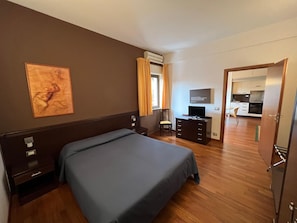 A hotel room with a bed, a desk, a television, and a view of the kitchen. - Residence San Martino (Messina)