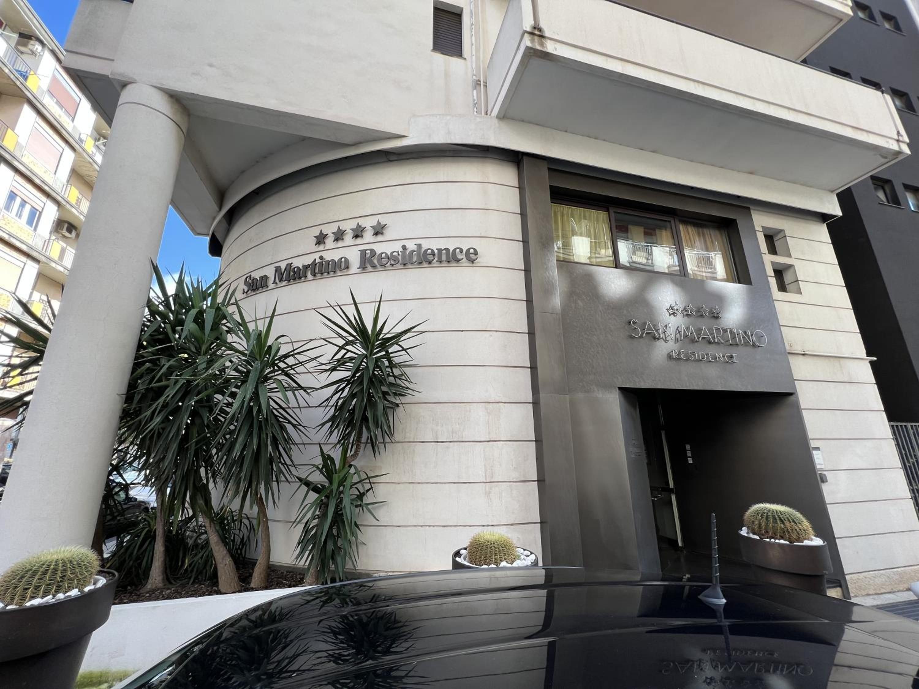 Un immeuble à la façade incurvée, une enseigne indiquant « Résidence de Saint-Marin », et une entrée moderne aux finitions métalliques.