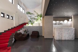 A modern hotel lobby with a red carpeted staircase, a reception desk, and a seating area with two sofas. - Residence San Martino (Messina)