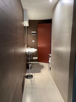 A narrow hallway with a sink, a trash bin, and a door leading to another room. - Residence San Martino (Messina)