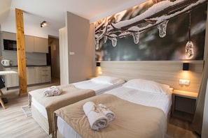 Habitación de hotel con dos camas, kitchenette y un amplio ventanal con vista a una rama nevada.