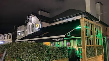 A bar with a green-lit exterior and a sign that reads 'RAISING THE BAR GUINNESS.'