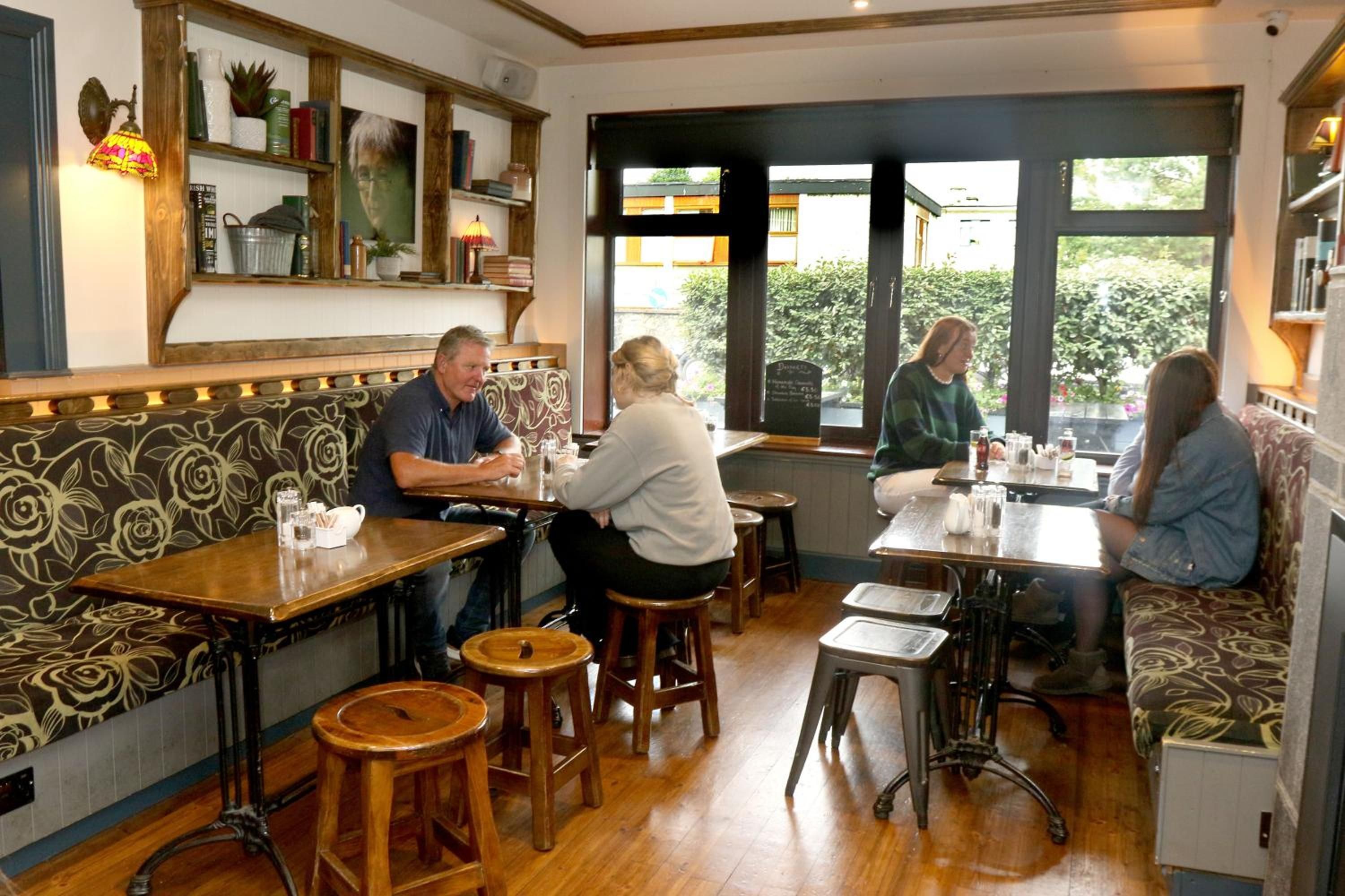 A restaurant interior with wooden tables and benches, a patterned wall, and a view through the windows.