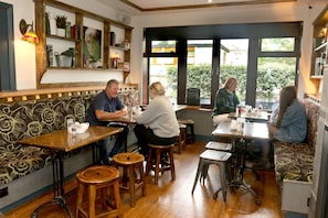 Interno di un ristorante con tavoli e panche in legno, una parete decorata e vista dalle finestre.