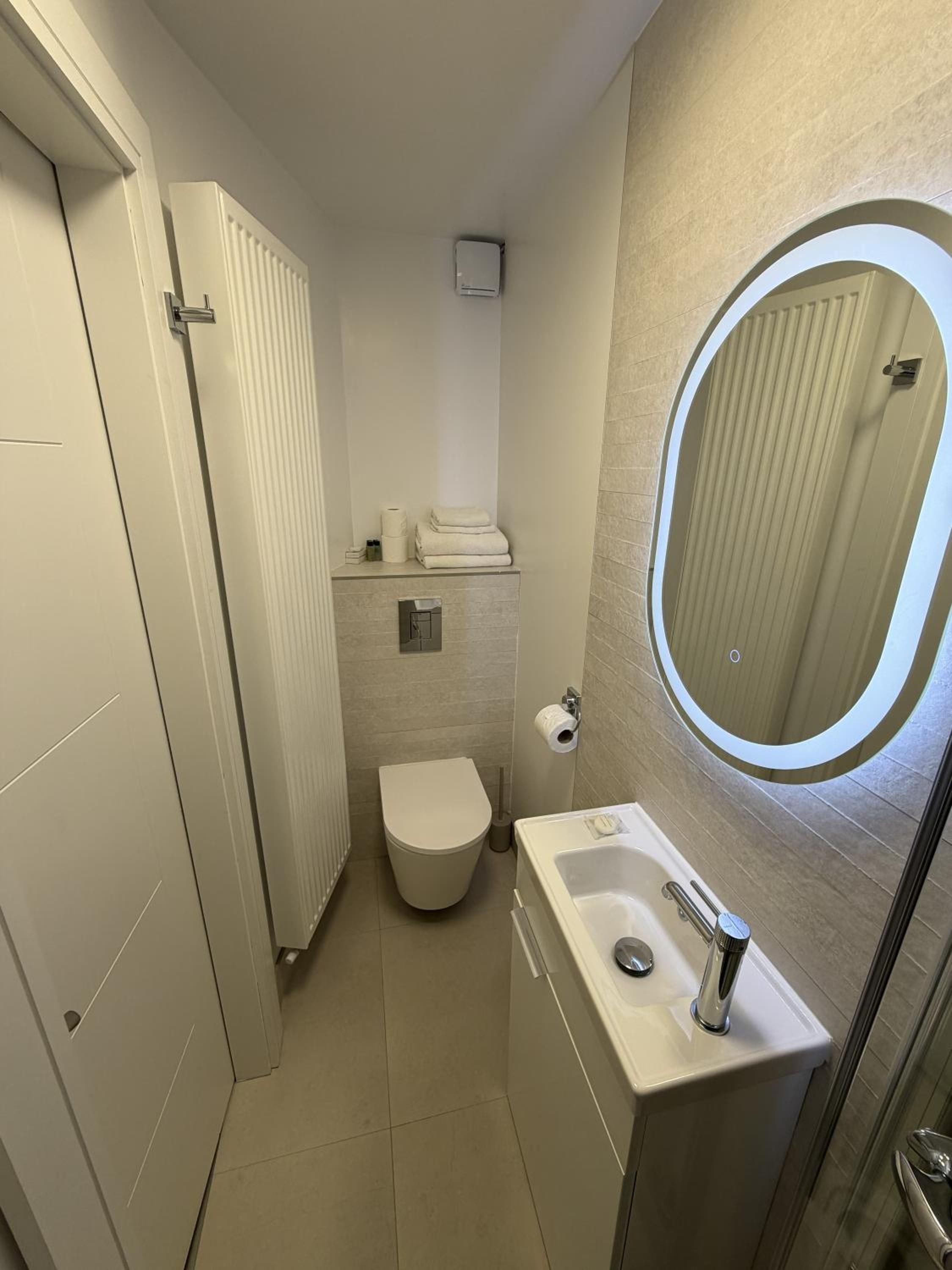 A compact bathroom with a toilet, a sink, a mirror, and a towel rack.