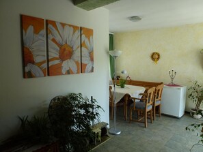 A dining area with a table, chairs, a floor lamp, and a refrigerator. There are two paintings on the wall and a potted plant in the foreground. - Landgasthof Faymann (Steinberg-Dörfl)