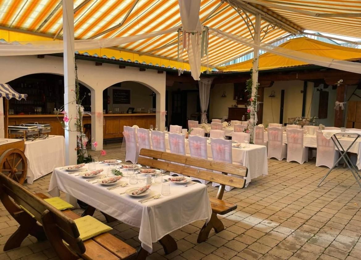 Un área de comedor al aire libre con mesas dispuestas para una comida, cubierta por un toldo a rayas y rodeada de bancos de madera.