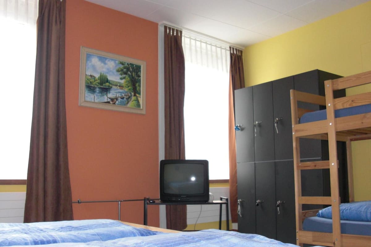 Ein Zimmer mit einem Etagenbett, einem Fernseher auf einem kleinen Tisch, einem Kleiderschrank und einem Bild an der Wand.