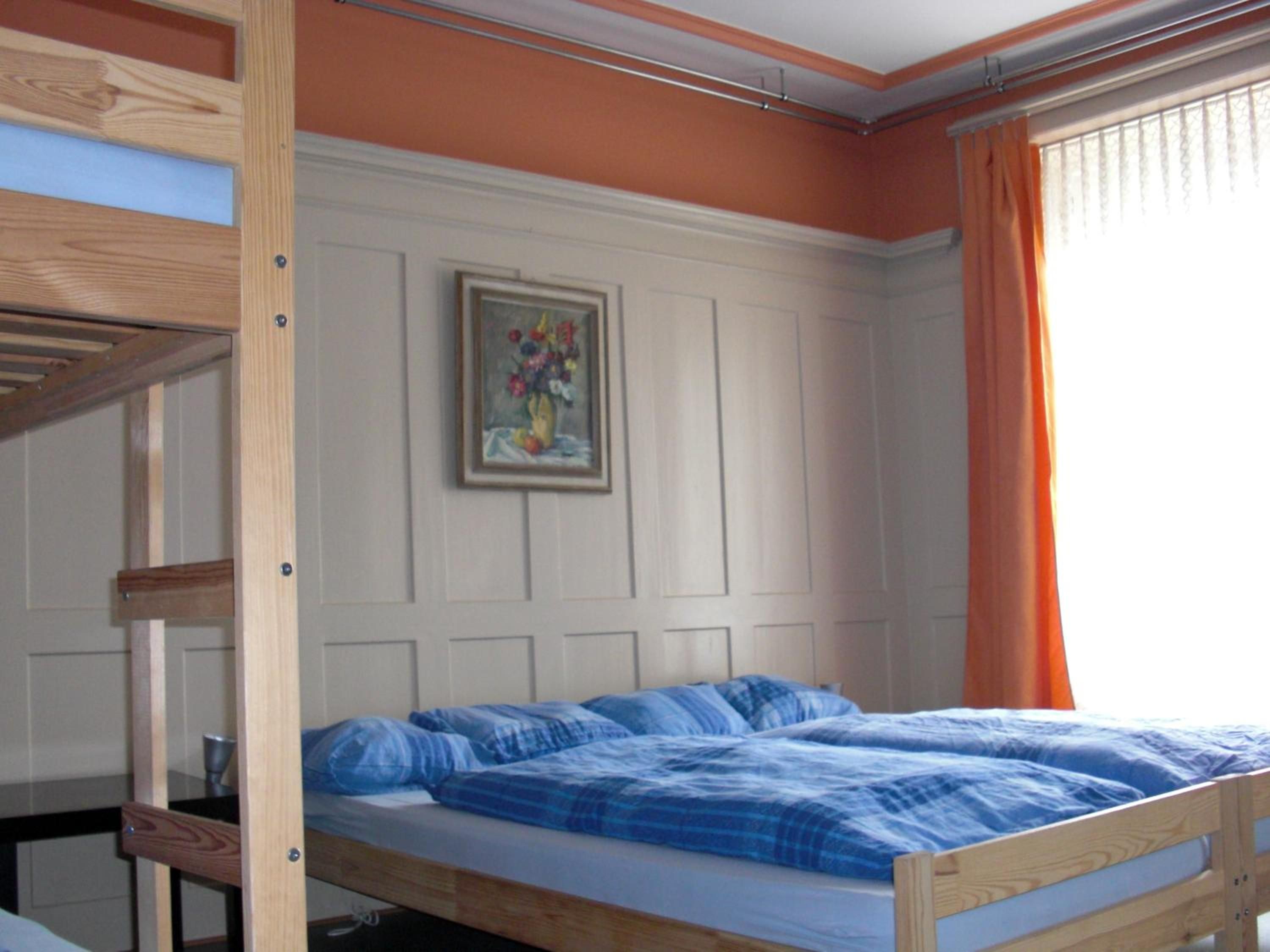 Ein Etagenbett mit einer blauen Decke, ein gerahmtes Bild an der Wand und ein Fenster mit Vorhängen.
